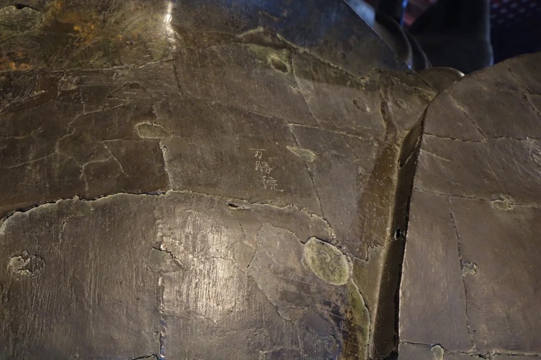 Bronze petal surface with incised figures.