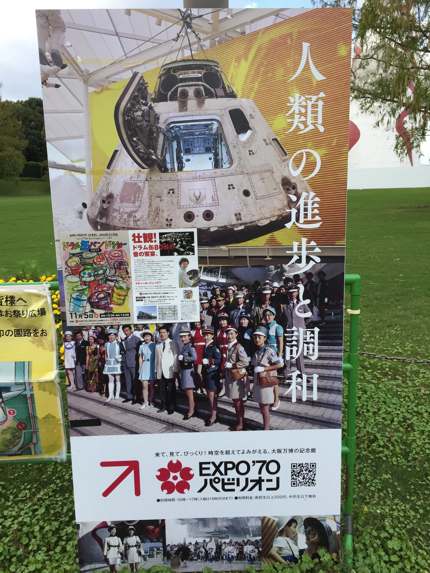Outdoor sign for the Expo &rsquo;70 Pavilion in Osaka, with a photograph of an Apollo command module and rows of pavilion staff in 1970s uniforms.